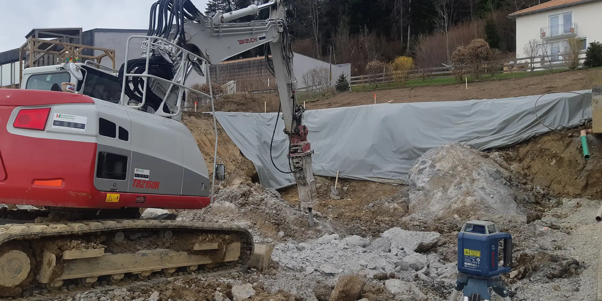 Kettenbagger mit Hydraulikhammer beim Aufbrechen von Felsmaterial auf einer Baustelle im Hang.