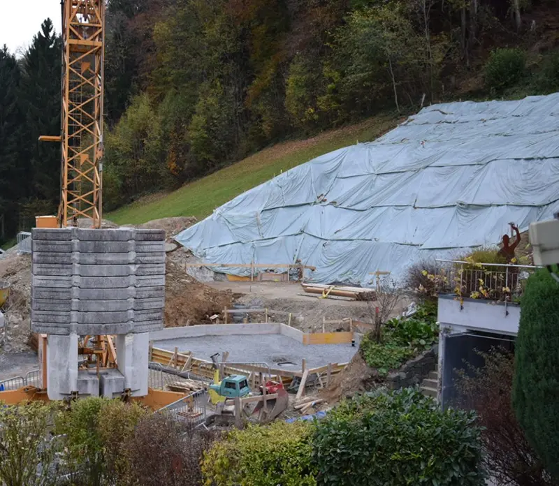 Großbaustelle mit Kran, Schalung und großflächiger Hangabdeckung mit Schutzfolie.