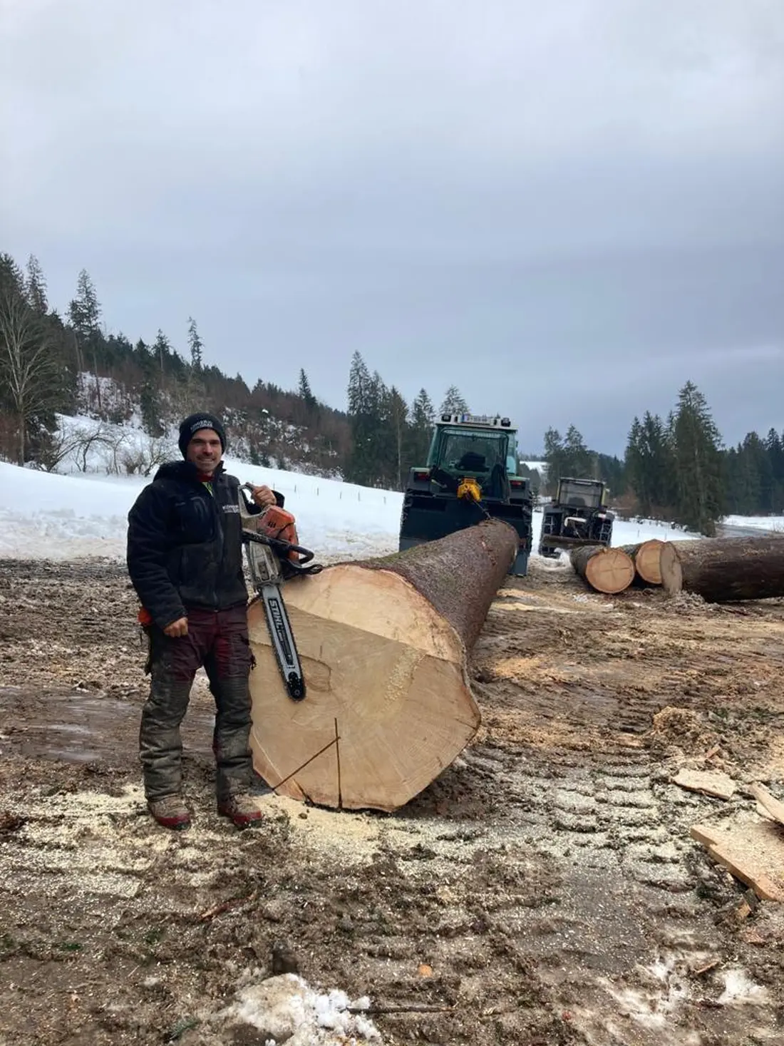 Forstarbeiter mit Motorsäge neben frisch geschnittenem Baumstamm im Winter