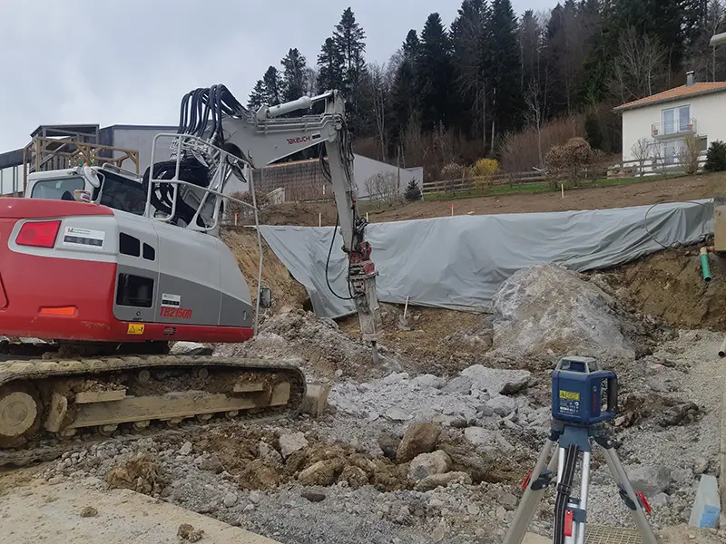 Kettenbagger mit Hydraulikhammer beim Aufbrechen von Felsmaterial auf einer Baustelle im Hang.