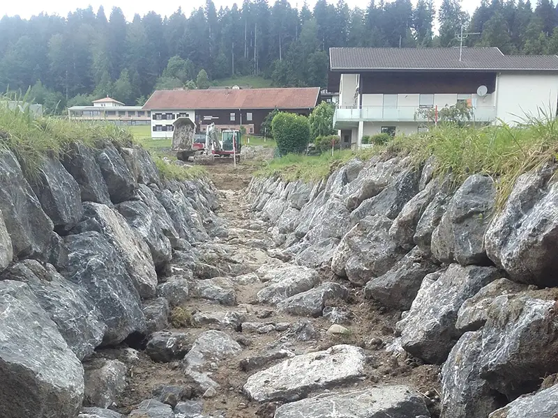 Steingefasster Entwässerungsgraben mit beidseitigen Natursteinmauern zwischen Wohnhäusern.