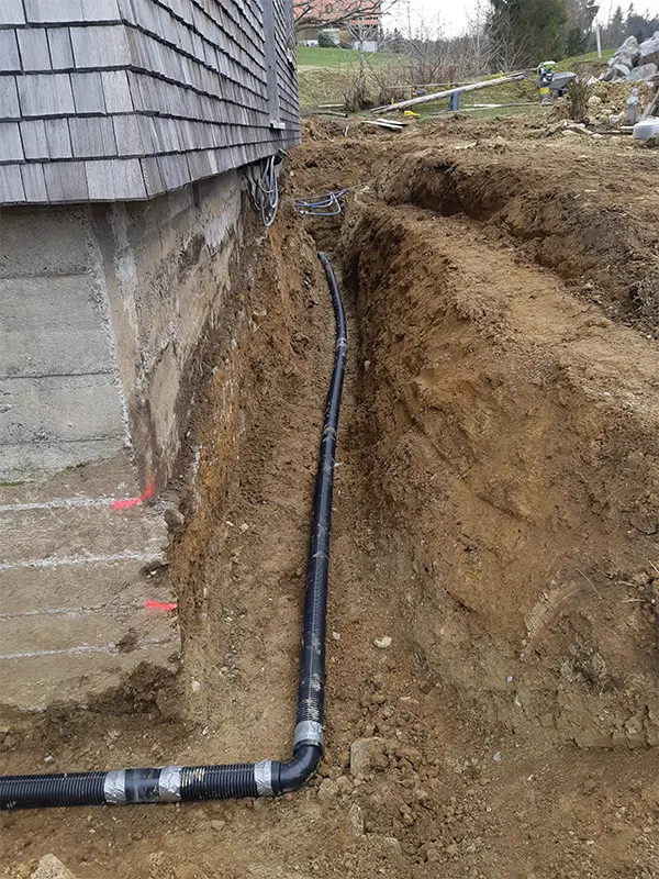 Offene Baugrube entlang eines Gebäudes mit verlegtem Drainage- und Entwässerungsrohr.