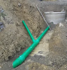 Verlegung von grünen Abwasserrohren in einer Baugrube mit Anschluss an einen Betonschacht.